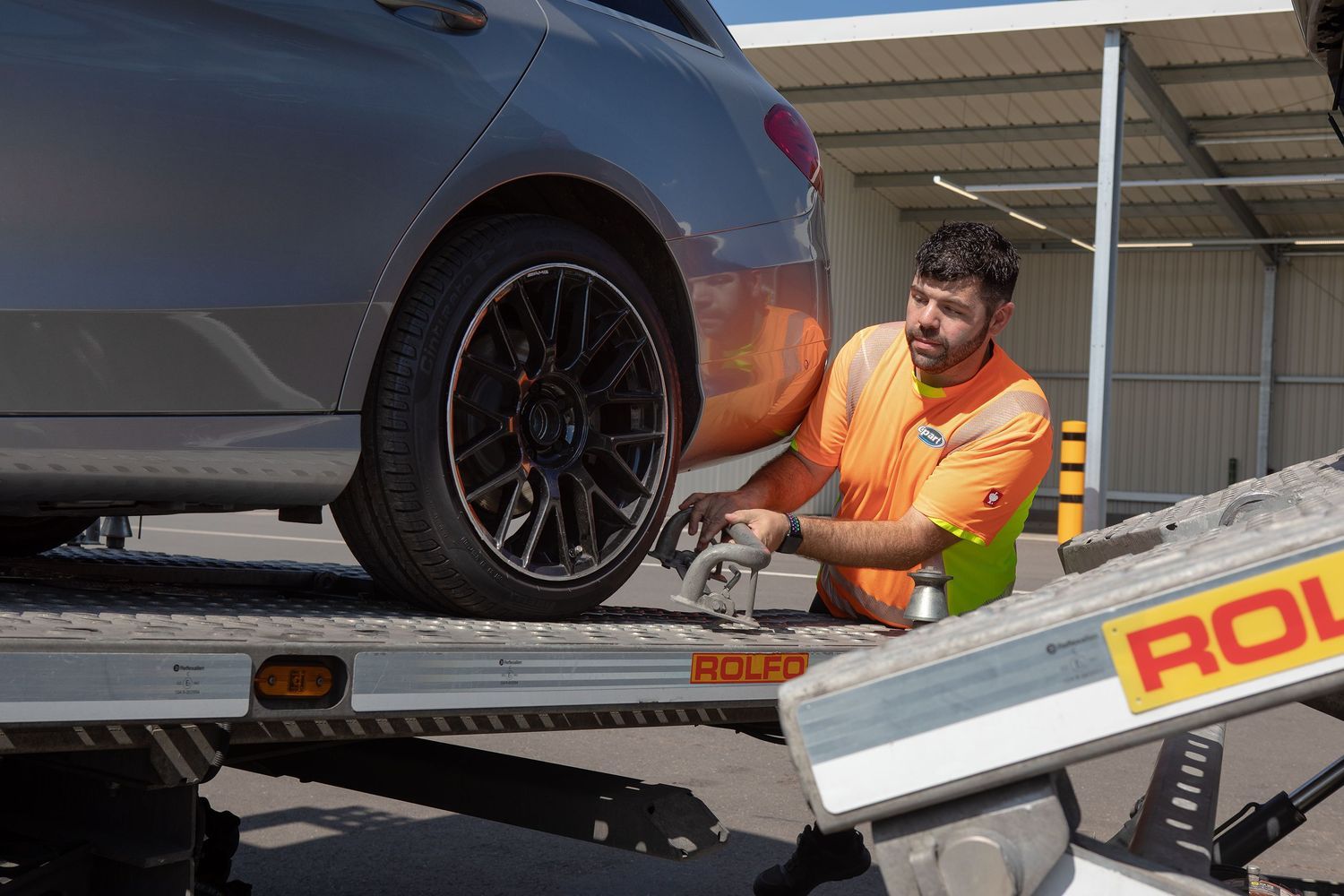 Ein Copart Yard Mitarbeiter löst eine Halterung am Hinterreifen eines Autos auf einem Transporter.
